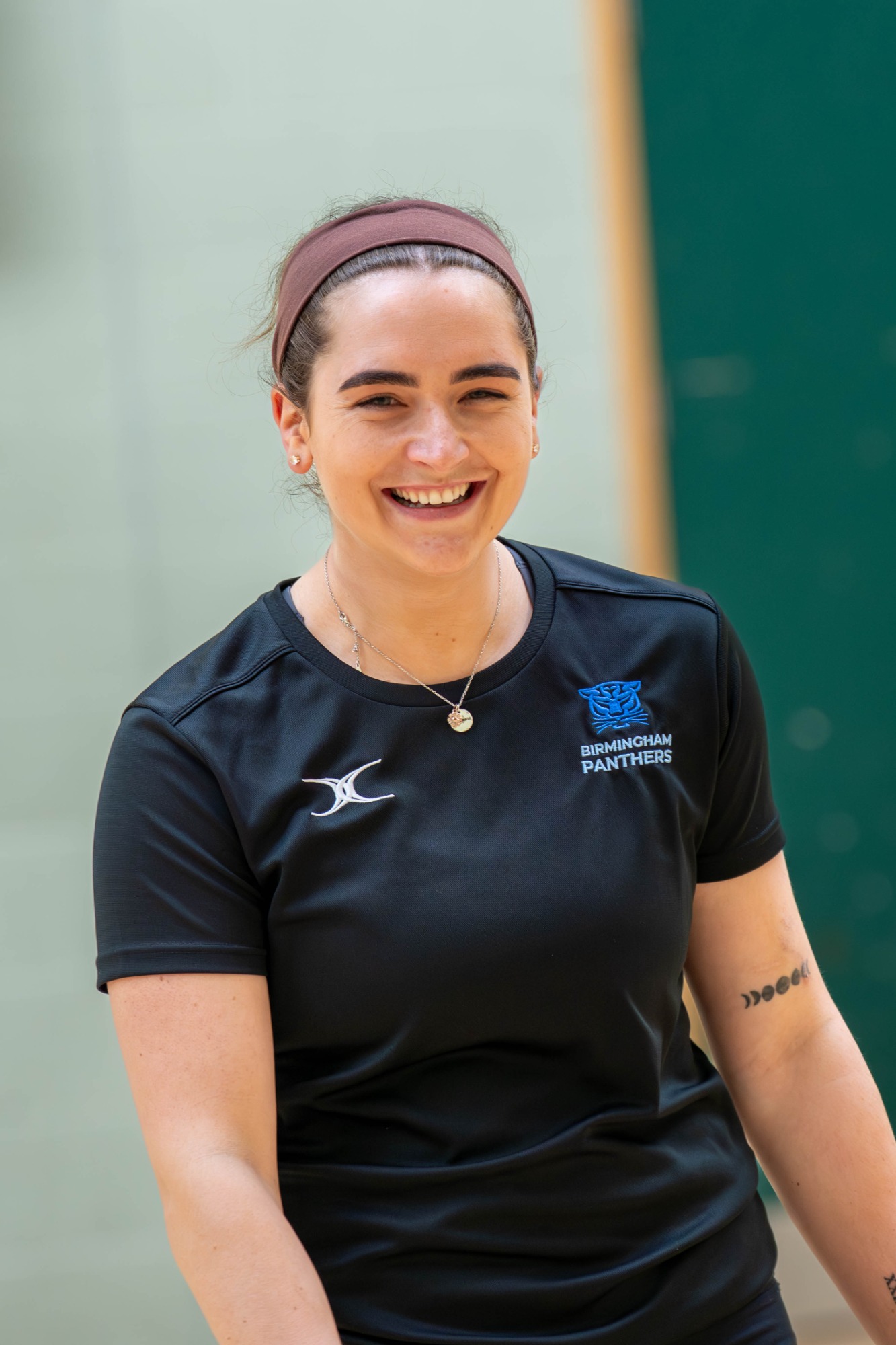 A smiling woman in sportswear, standing indoors, with a green background.