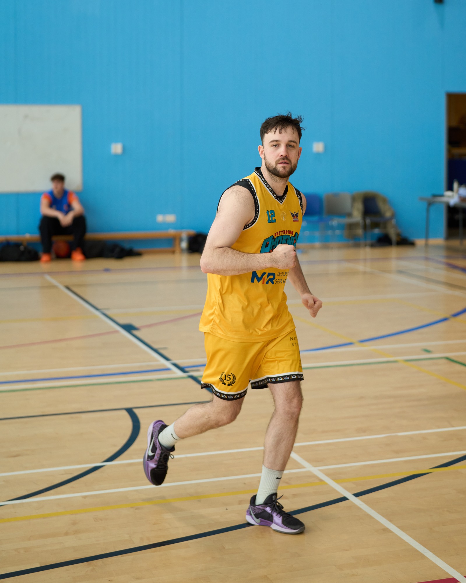 A basketball player in a yellow uniform runs on a court.