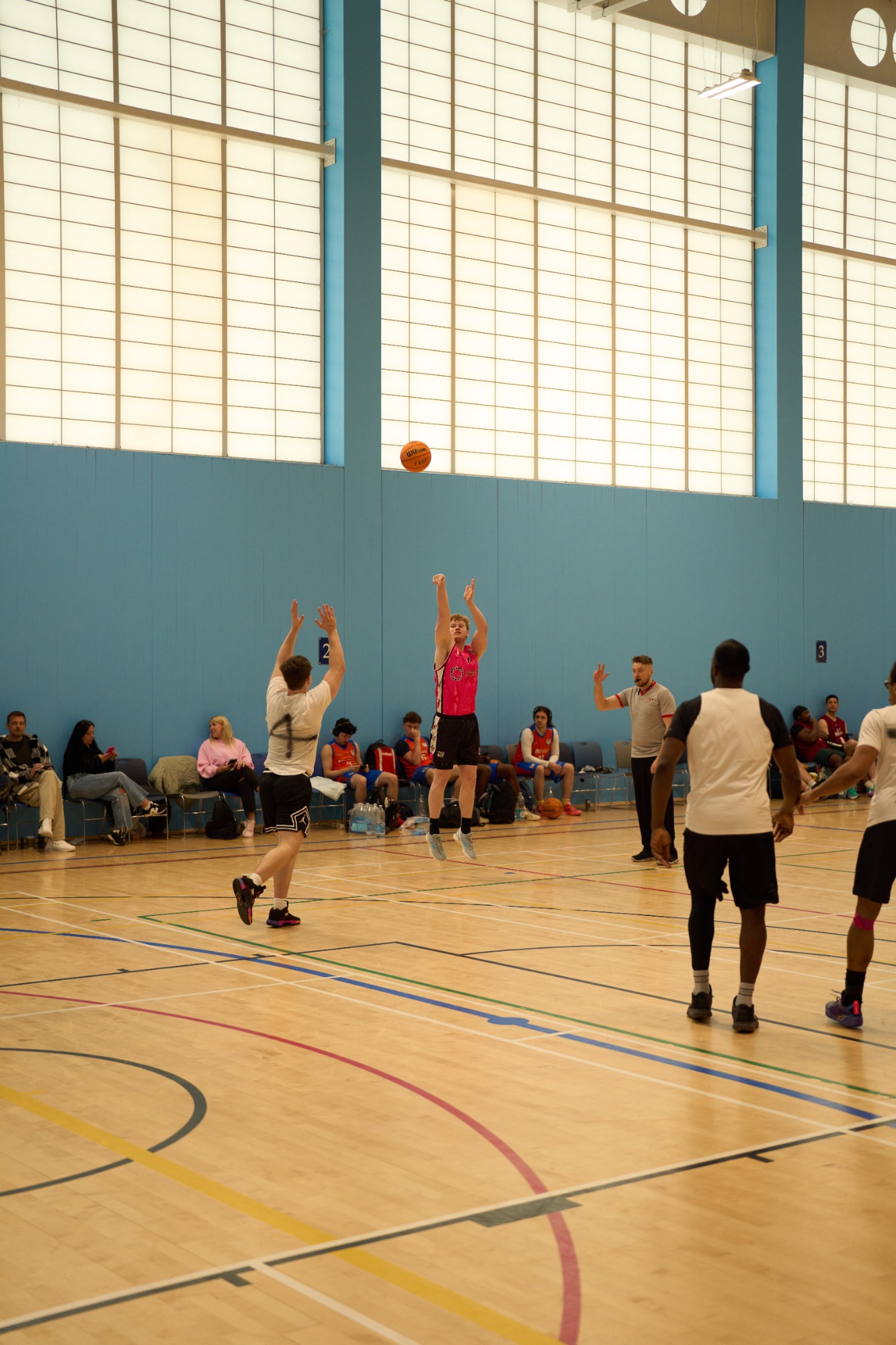 A basketball player jumps to shoot while others watch and wait on the court.