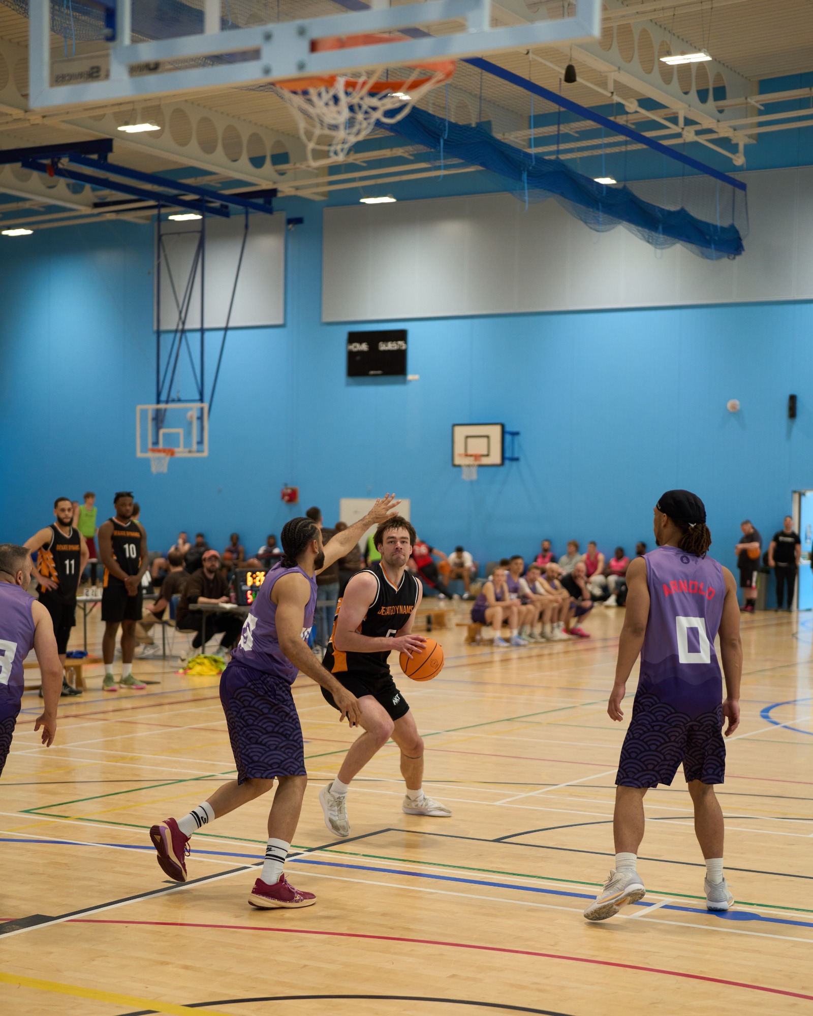 A basketball player in black prepares to shoot, surrounded by opponents in purple jerseys.