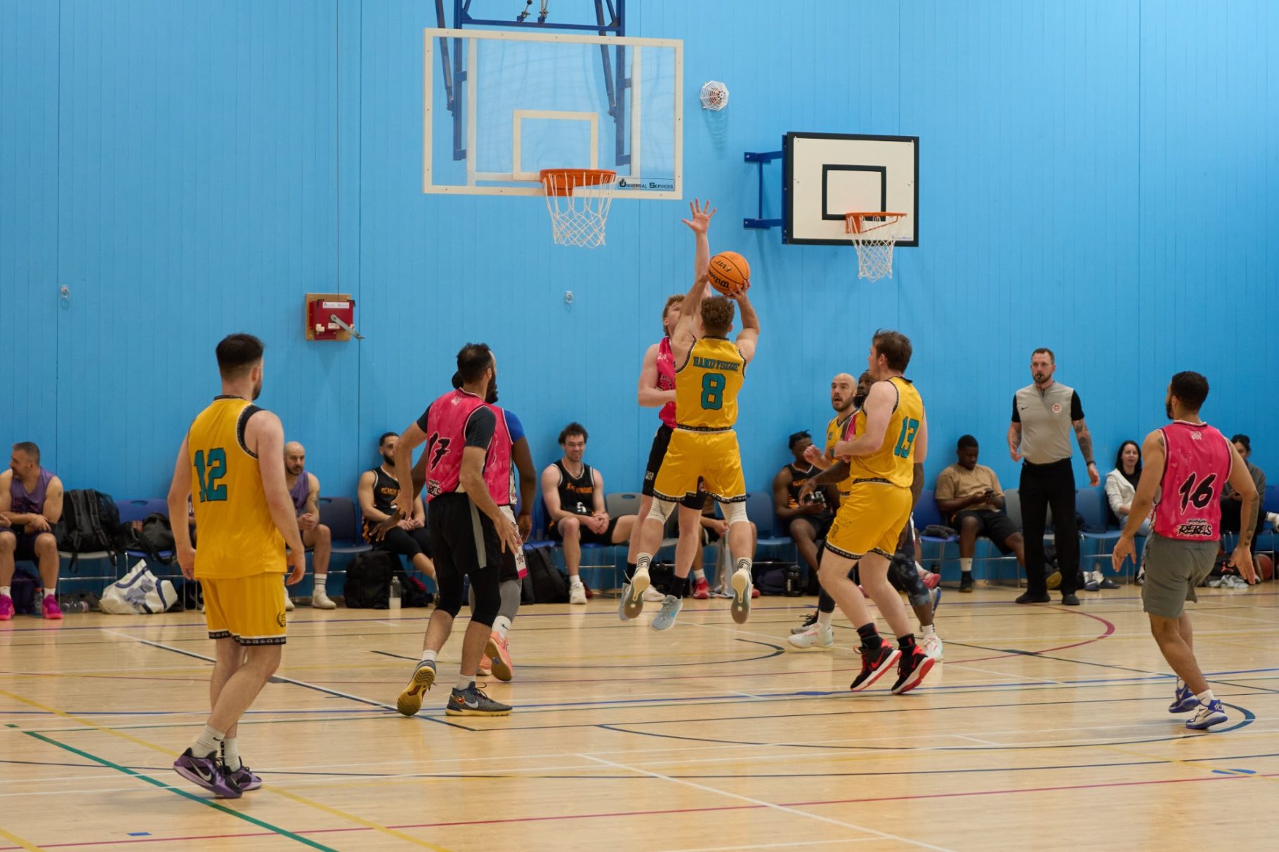 A basketball player jumps to shoot during a competitive match in a gym.