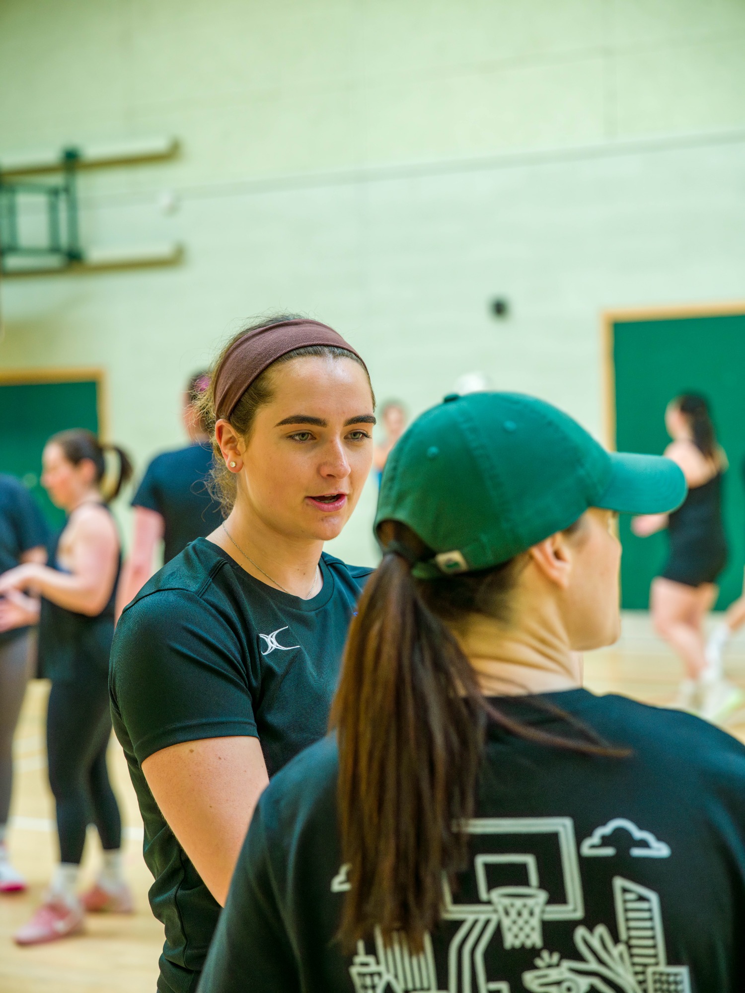 Two young women engaged in conversation during a netball practice session.