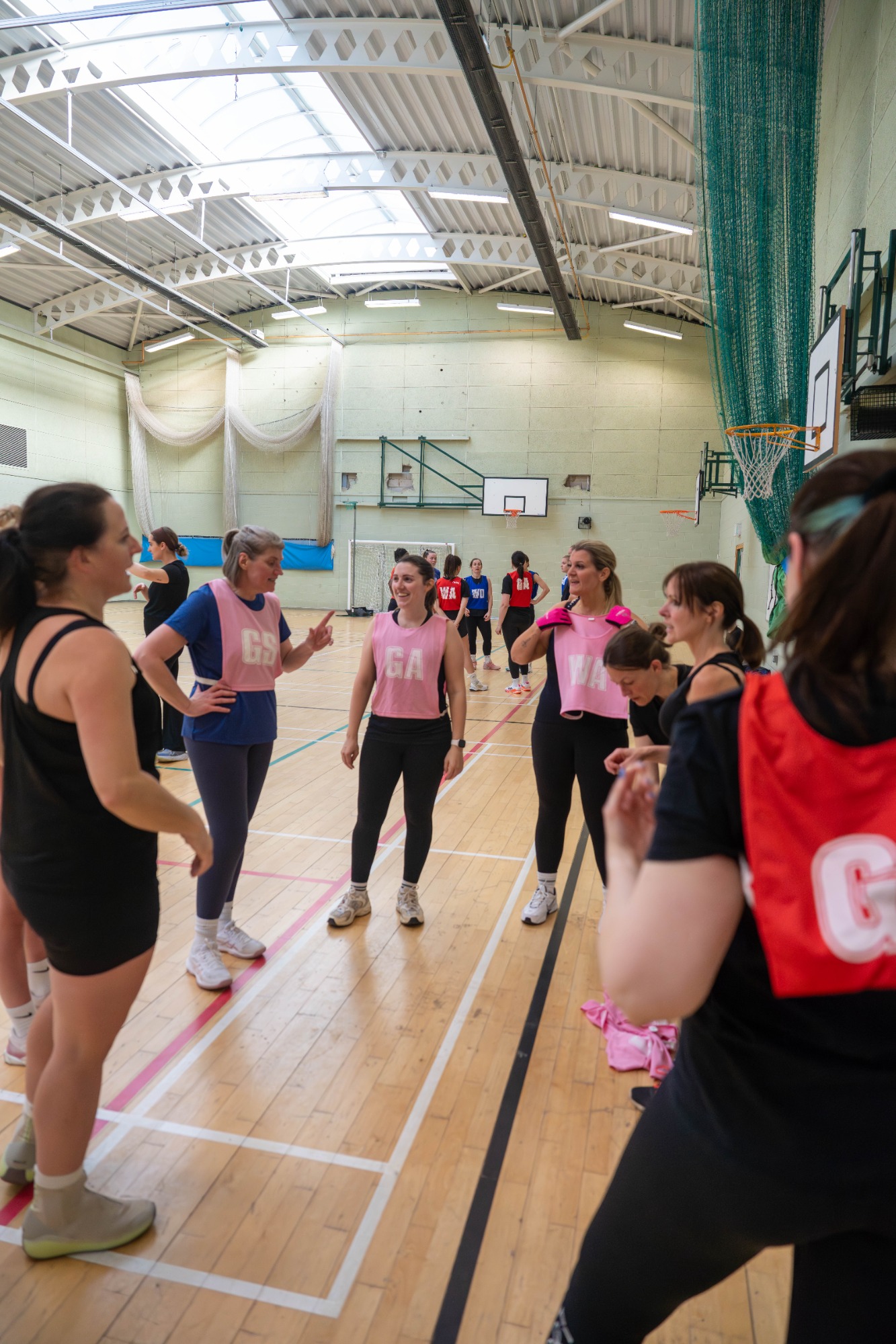 Women in a sports hall discussing strategies during a netball training session.