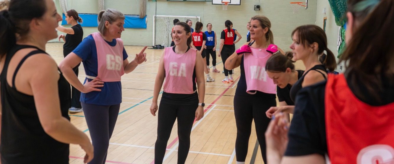 Group of women in sports attire chatting during a netball practice session.