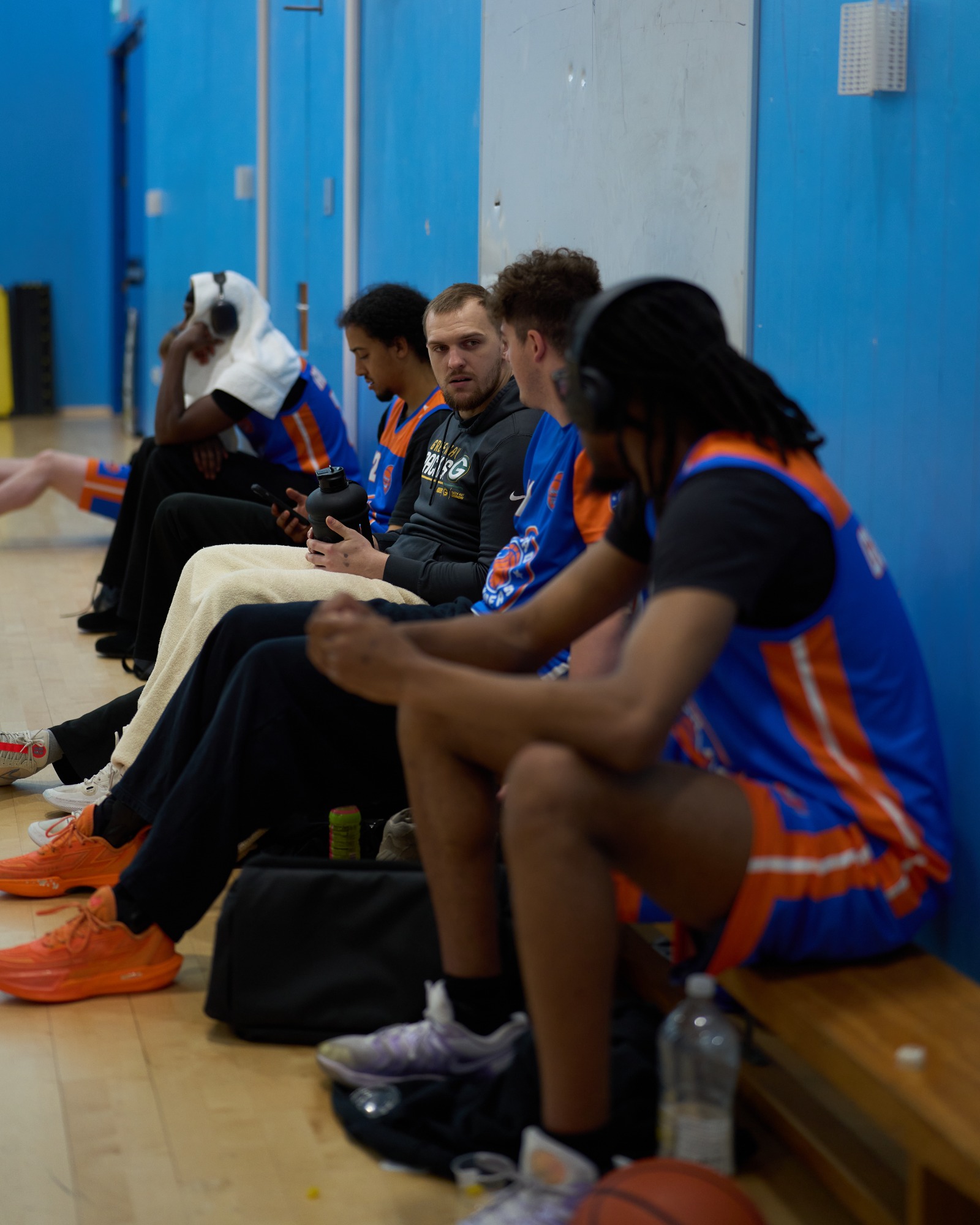 Basketball players seated on a bench, wearing team gear and resting.