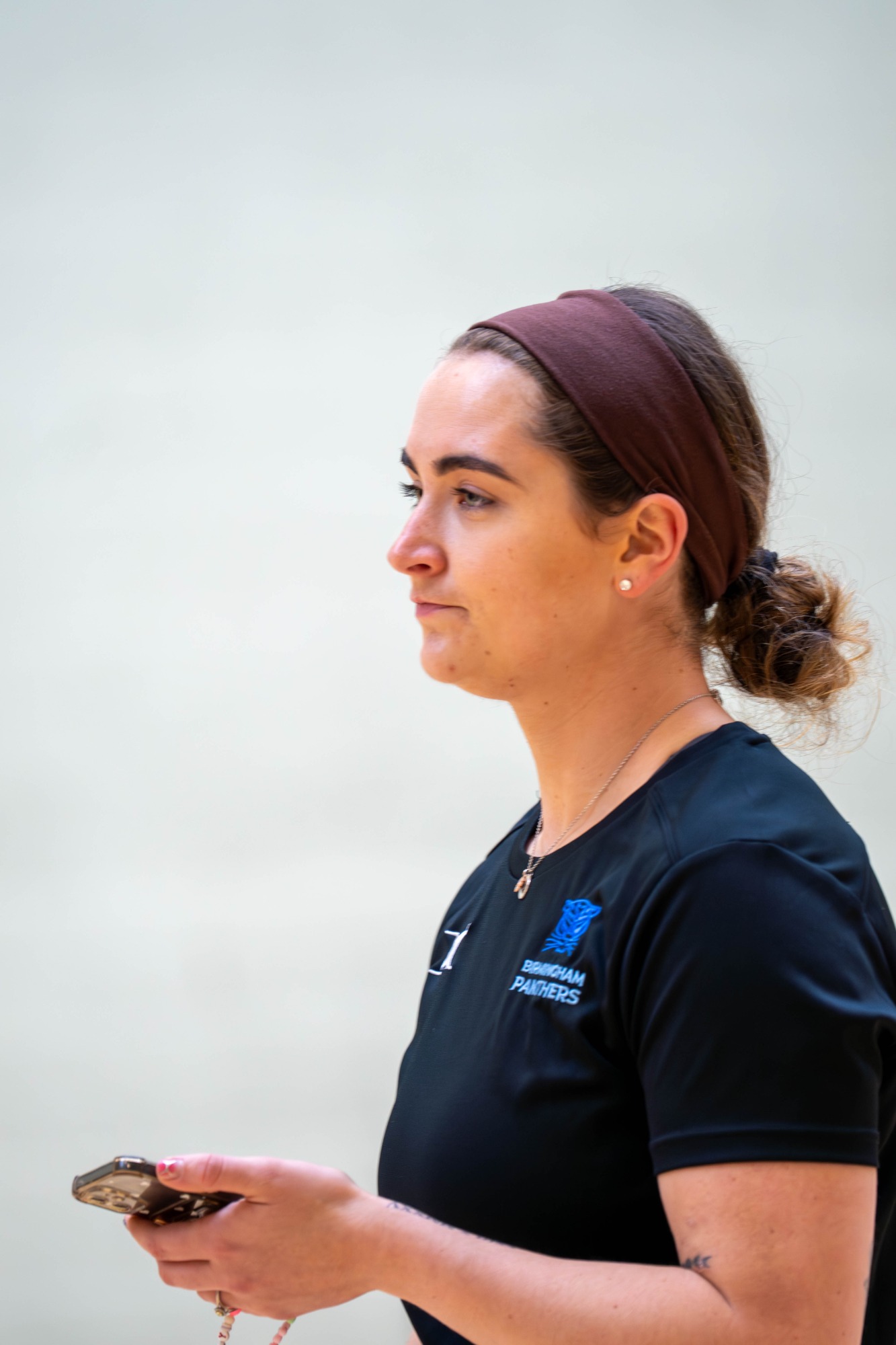 A woman with a headband, holding a phone, looking thoughtfully to the side.