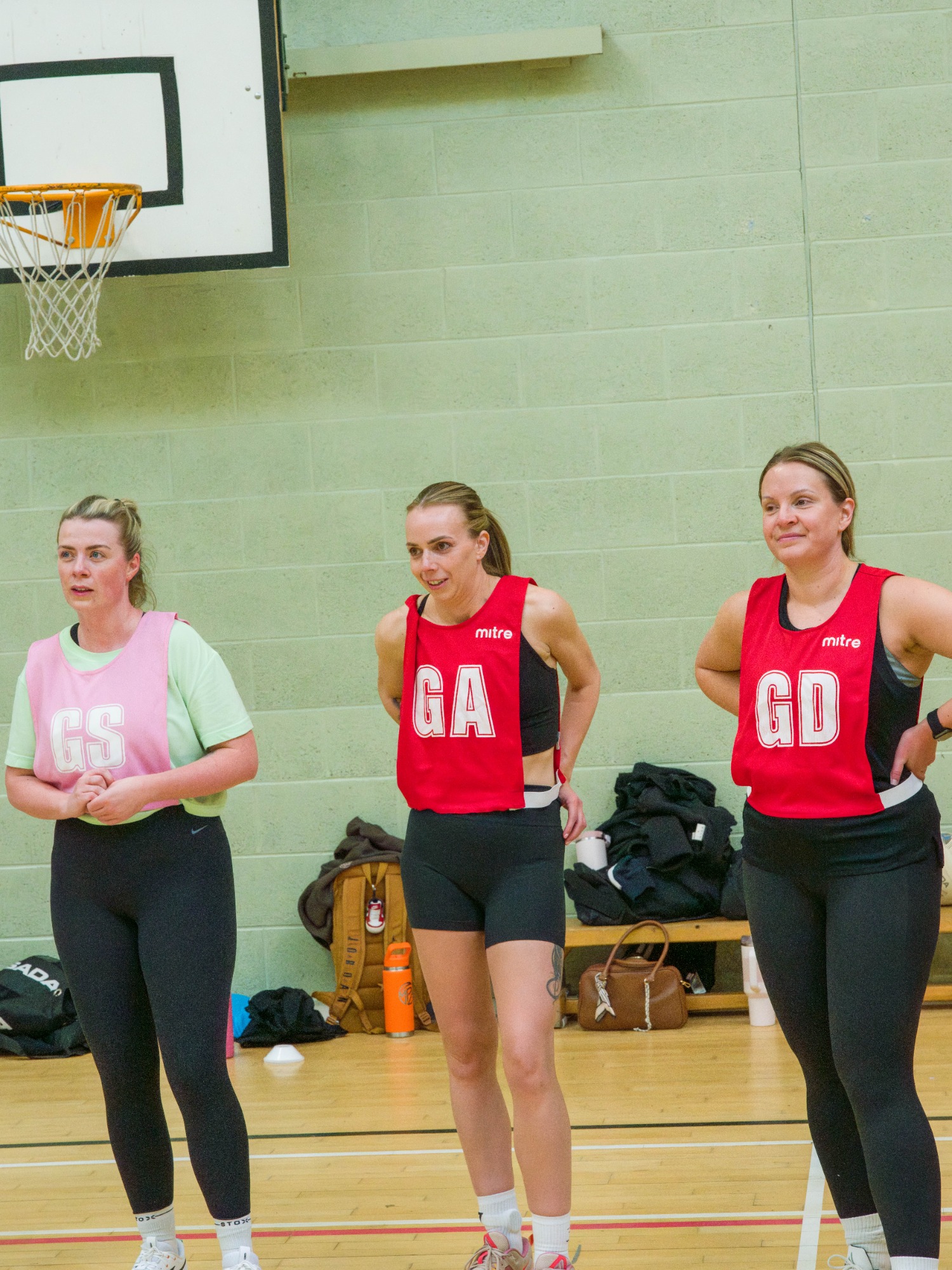 Three women in sportswear stand on a netball court, wearing positions GS, GA, and GD.