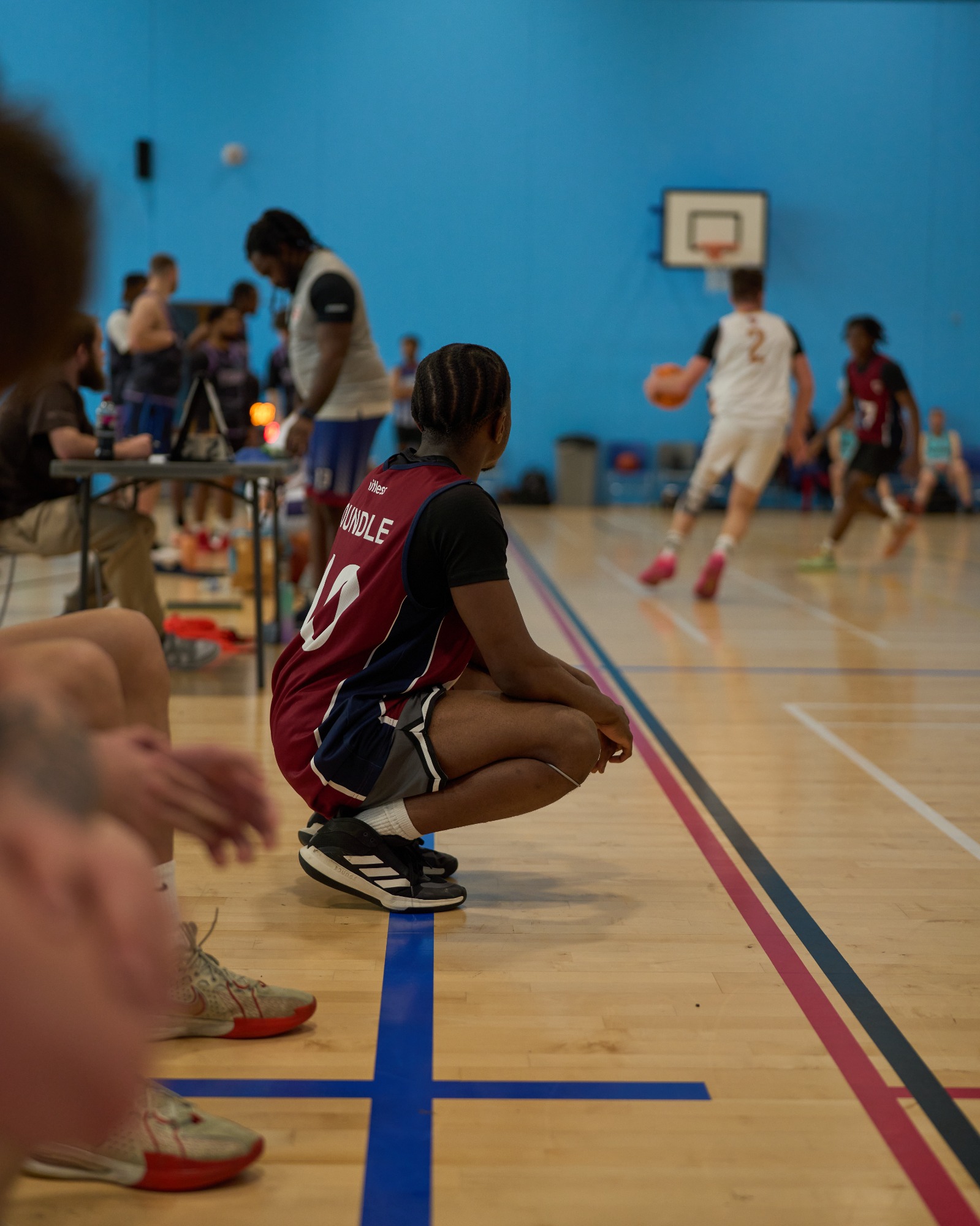A player crouches on the sideline while another team member dribbles the ball.