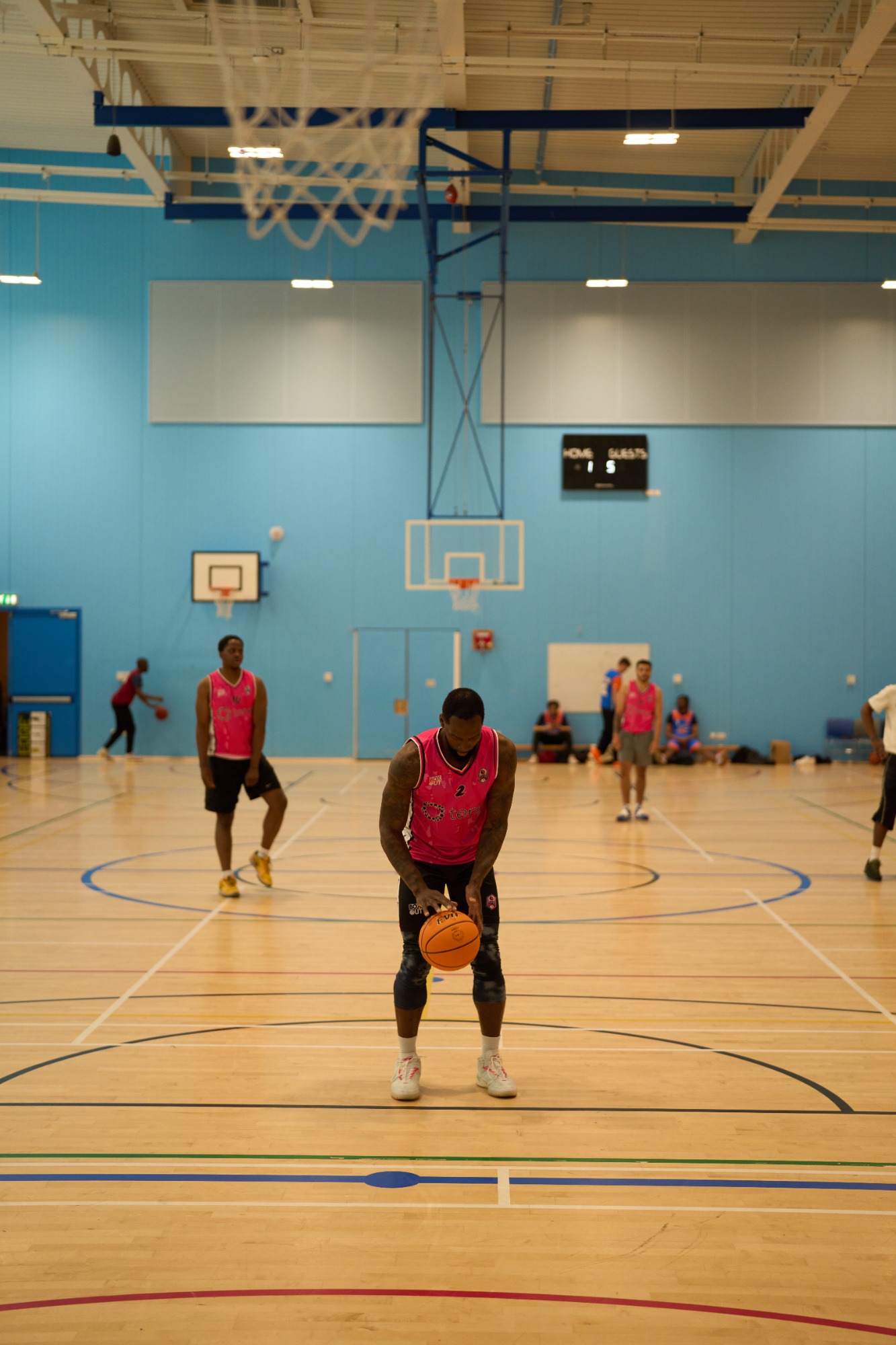 Basketball players practising in a gym, wearing pink jerseys and preparing for a shot.