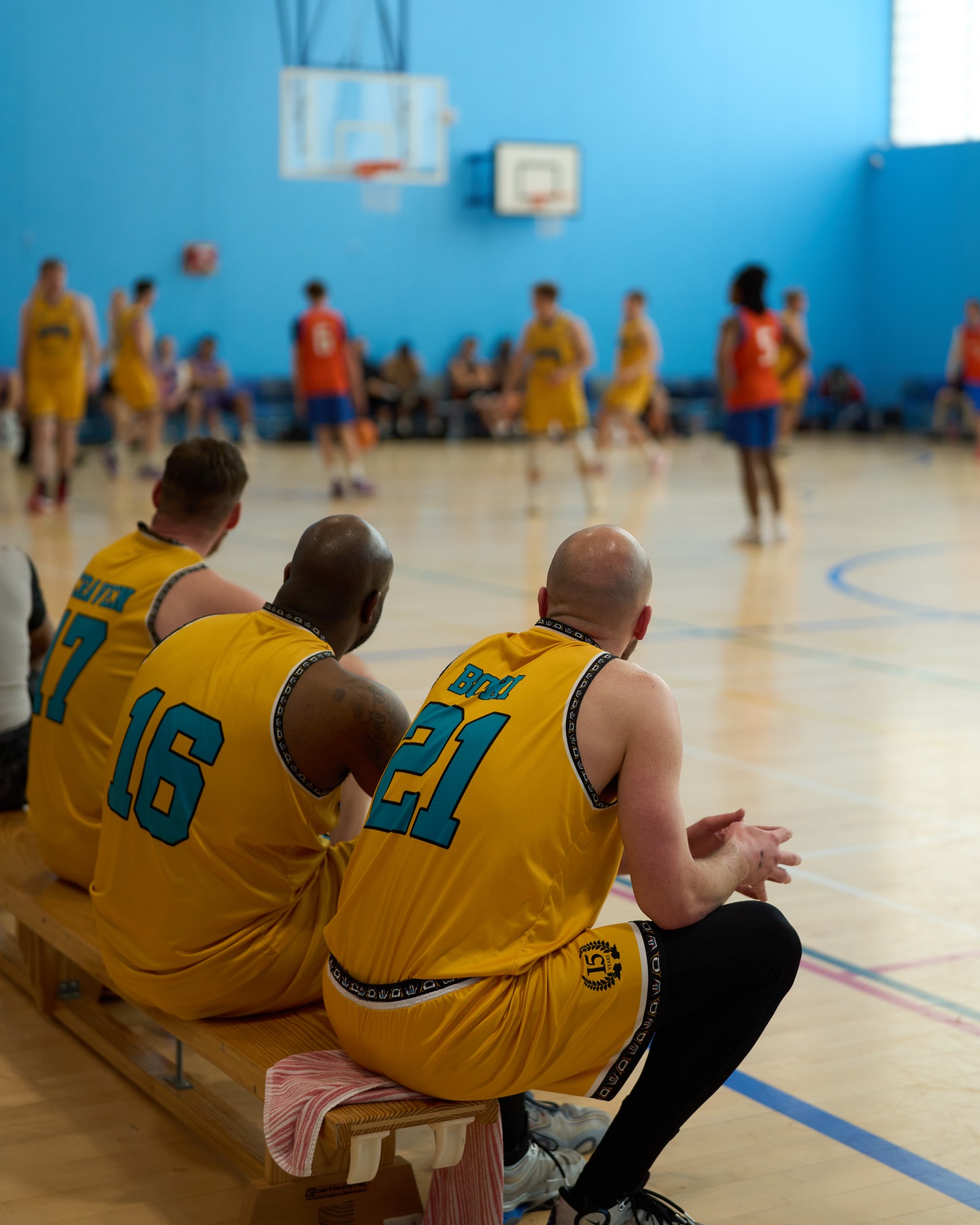 Three basketball players in yellow jerseys sitting on the sidelines, watching a game.