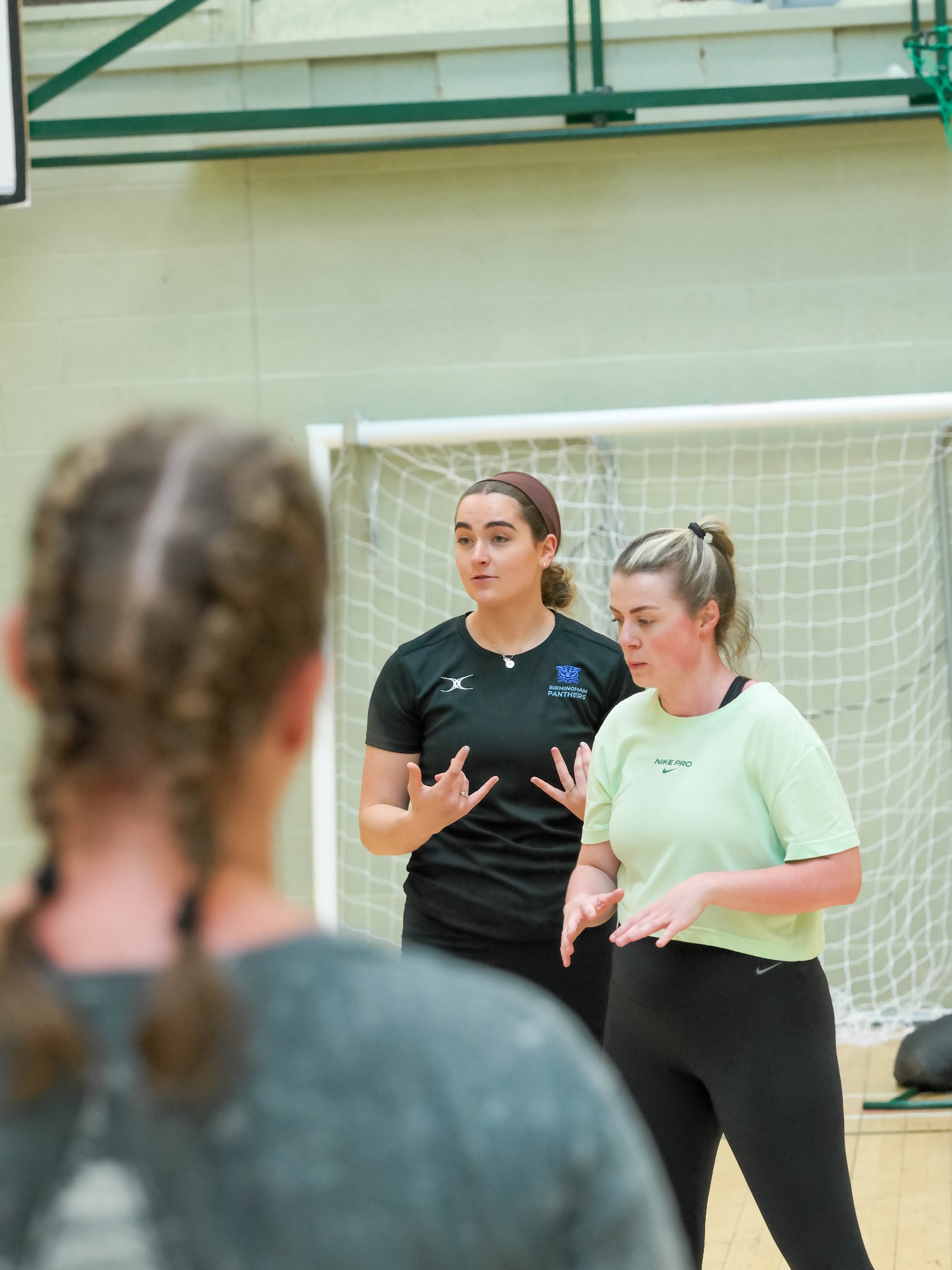 Two women discussing strategies in a sports hall, one gesturing while speaking.