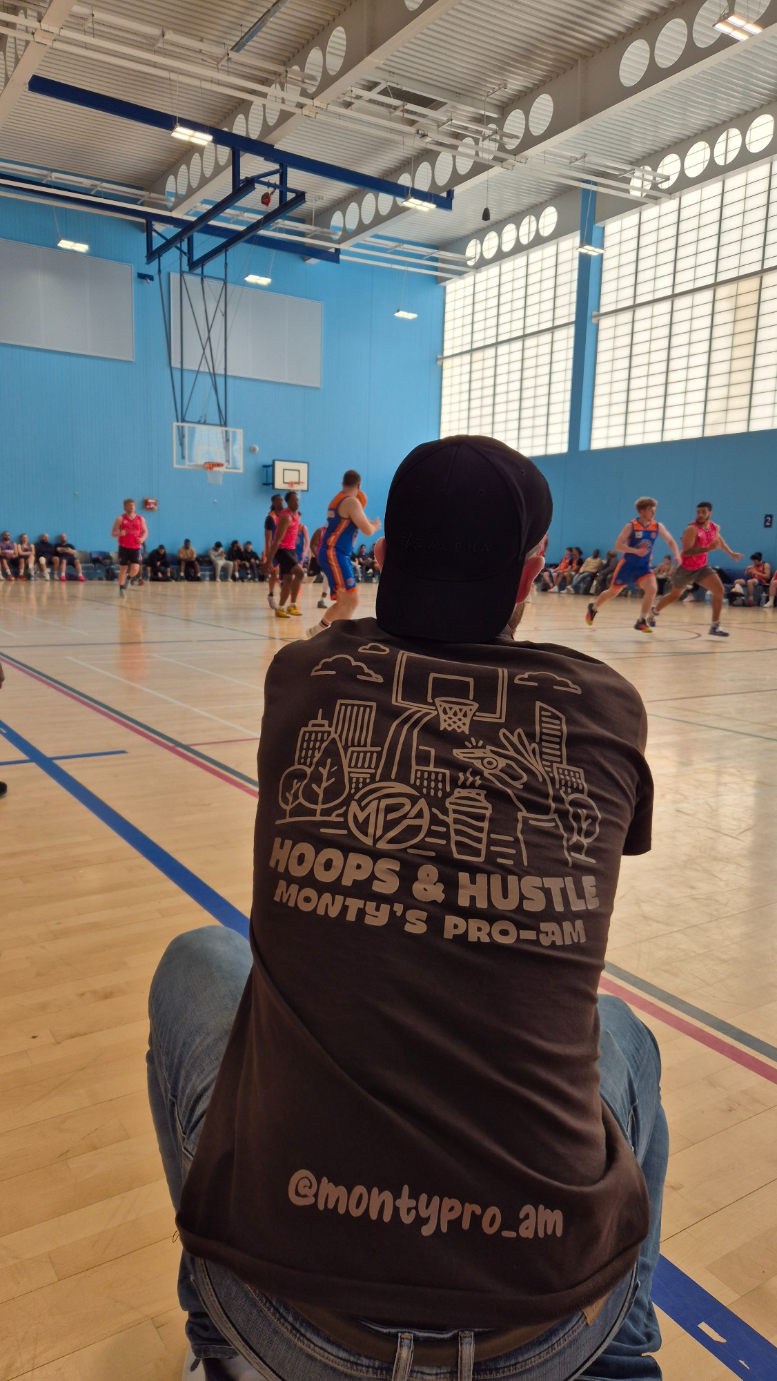A person sitting on the floor watching a basketball game in a gymnasium.