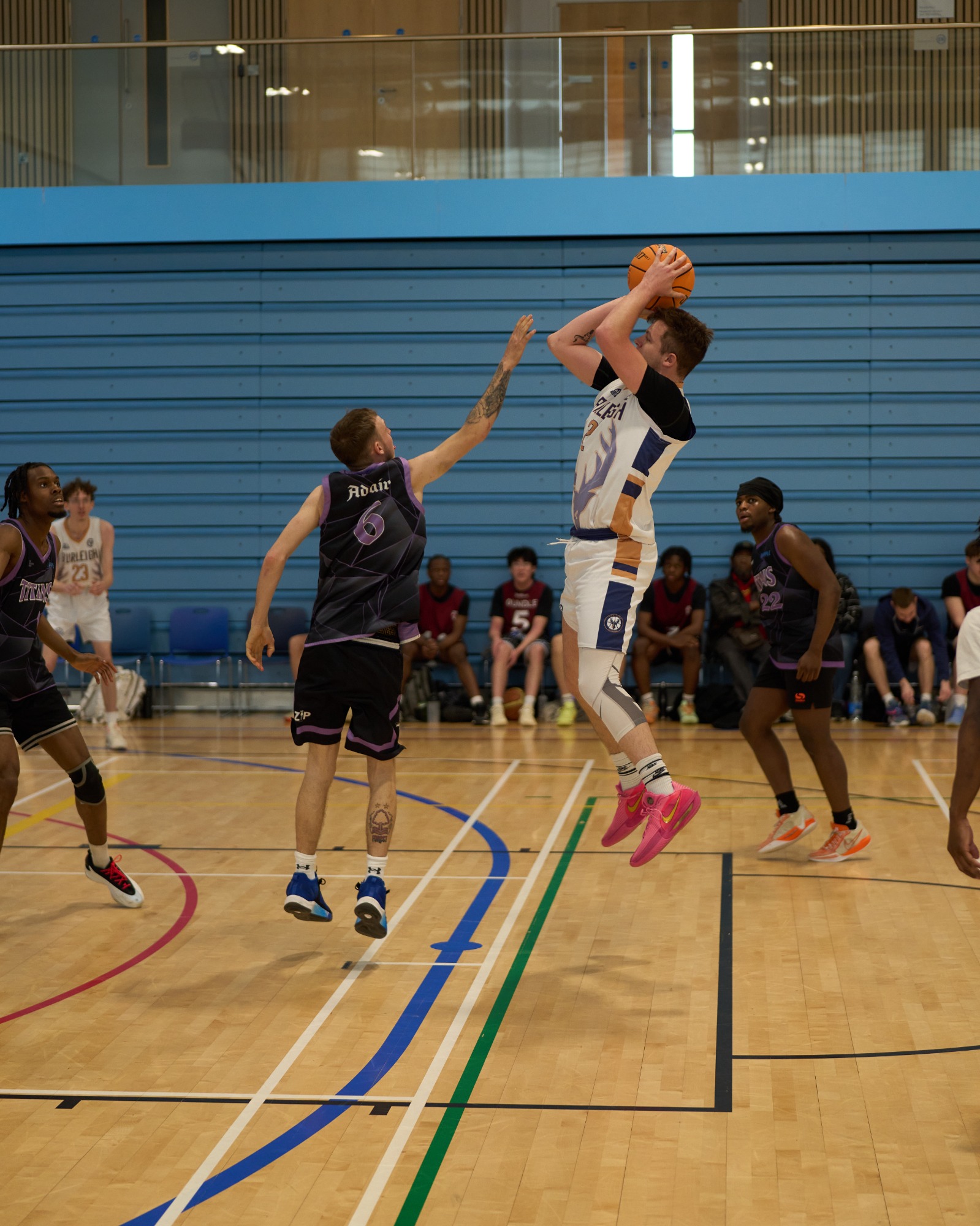 Side on of a mid air basketball jump shot with defender hand in their face.