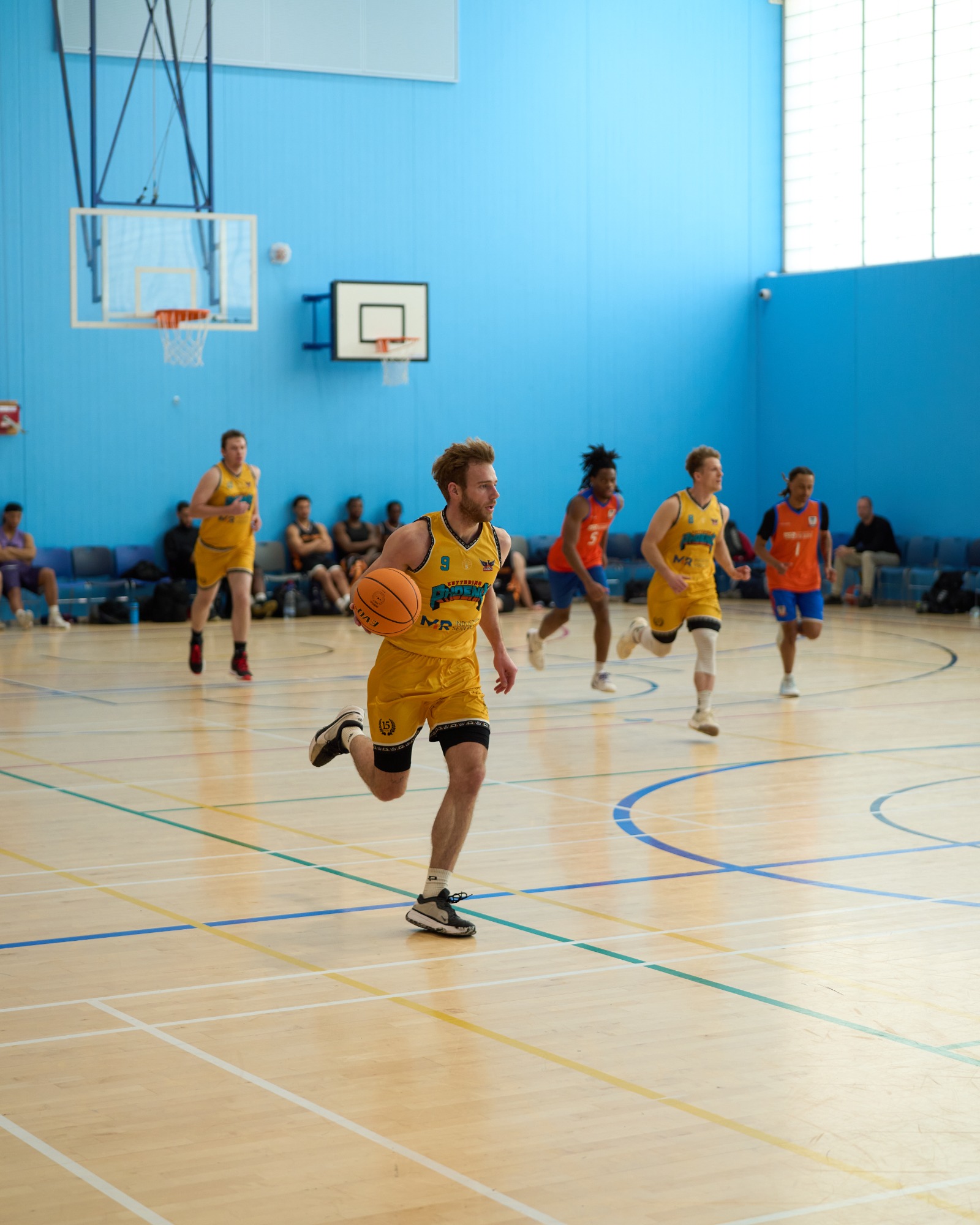 A basketball player in yellow jersey dribbles the ball during a game in a gym.