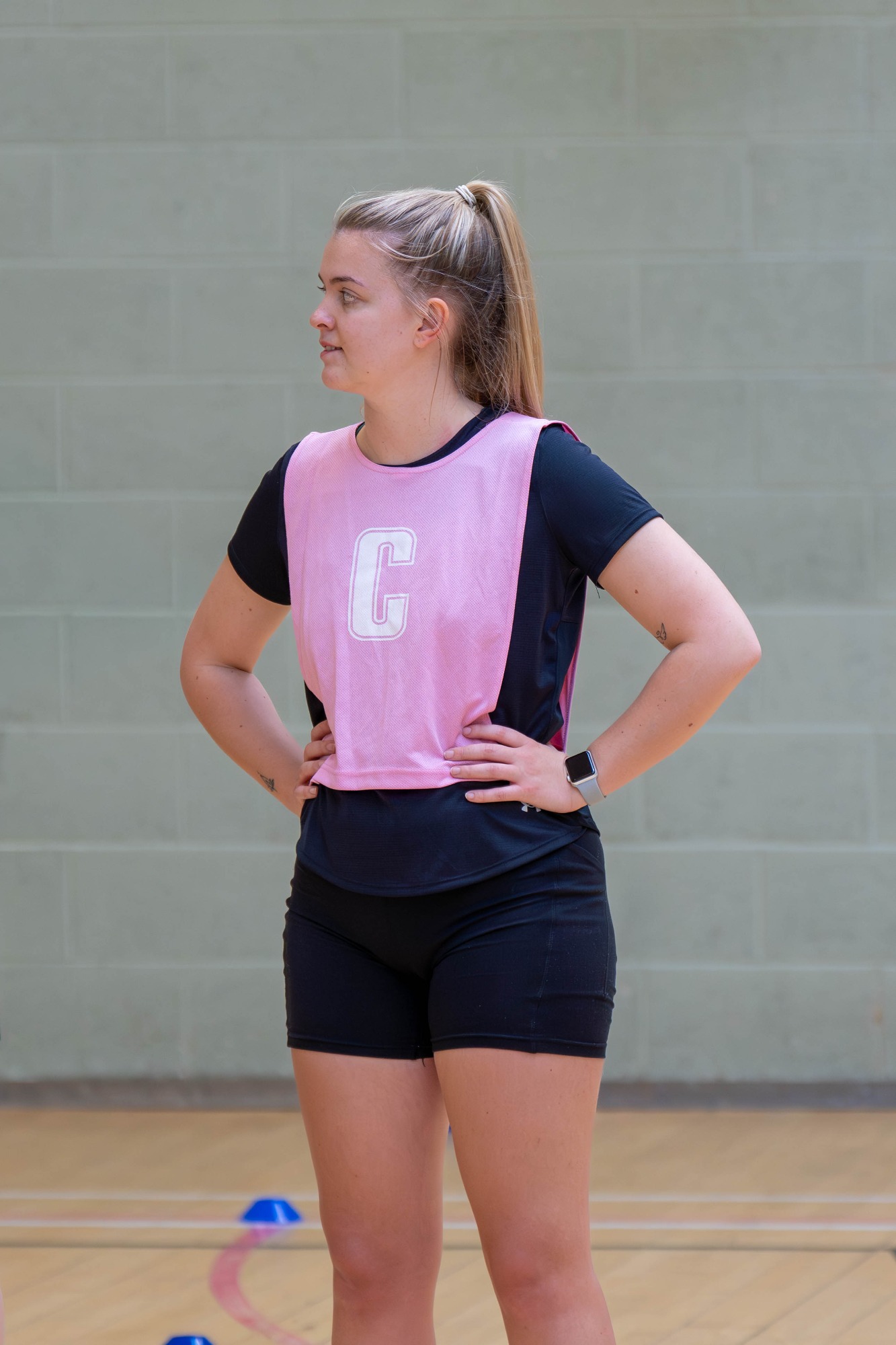 A young woman wearing a pink bib with a "C" stands confidently in a sports setting.
