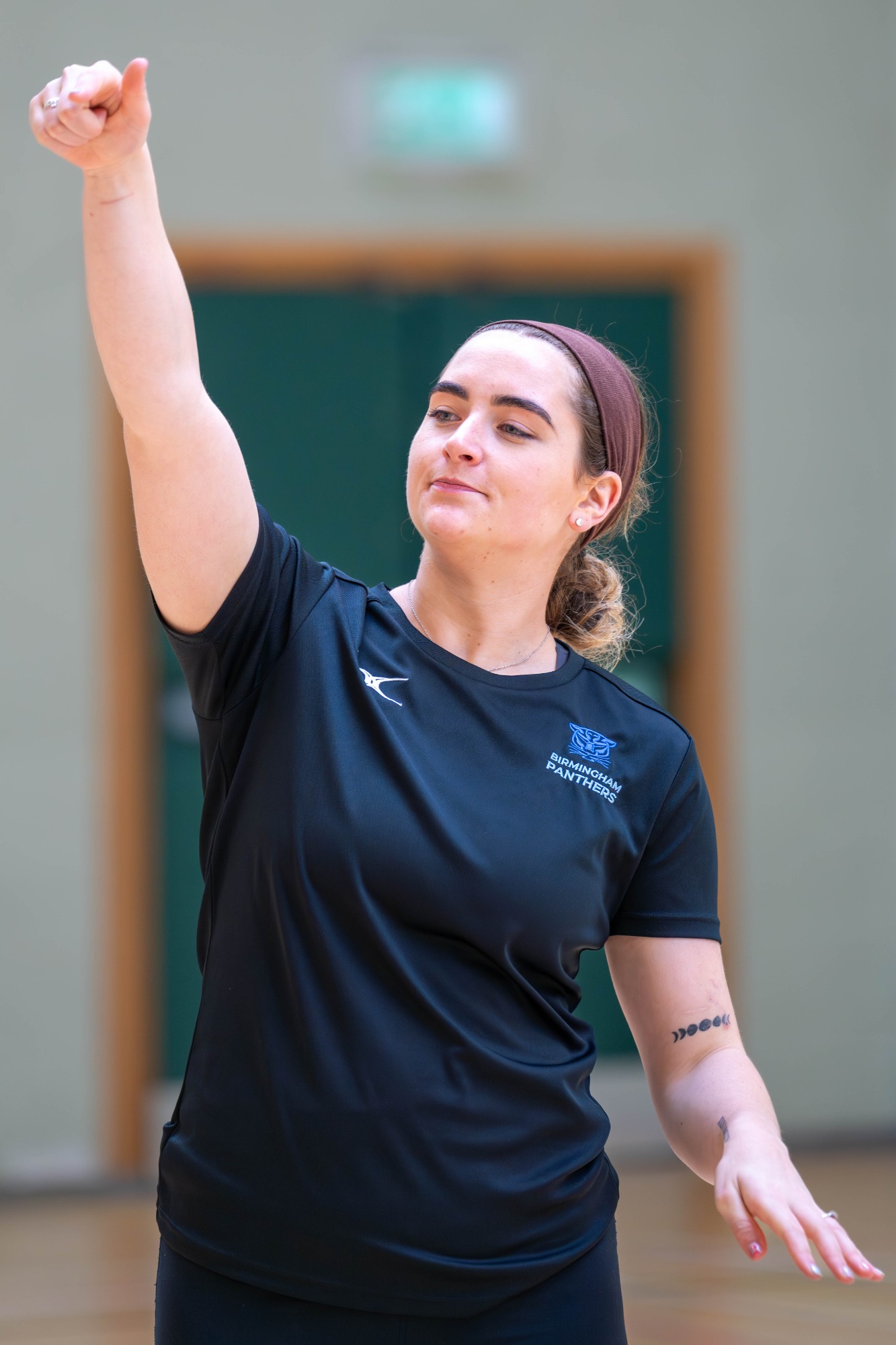 A woman in sports attire raises her arm confidently, signaling during a game.