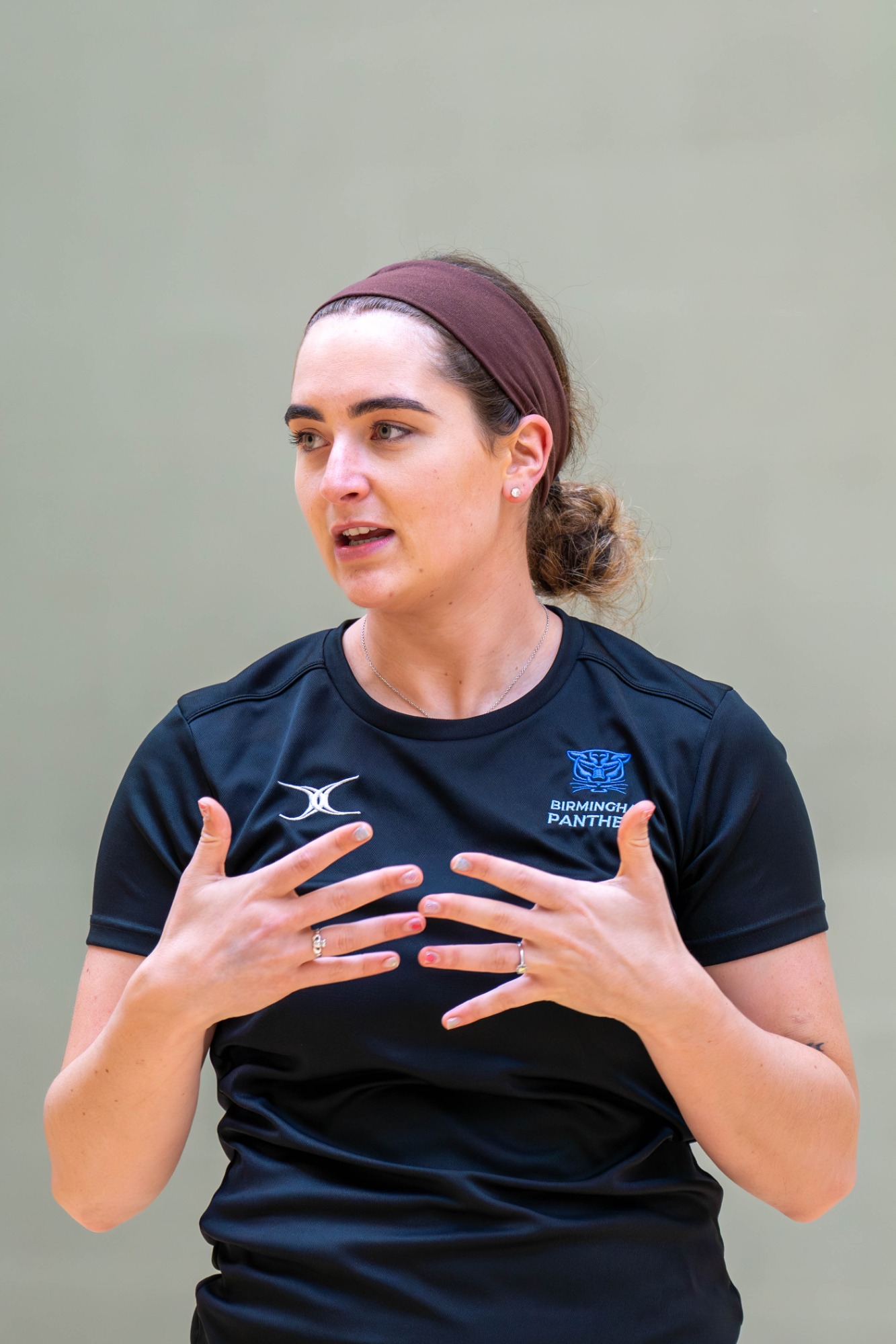 A woman in a black shirt gestures while speaking, with a focused expression.