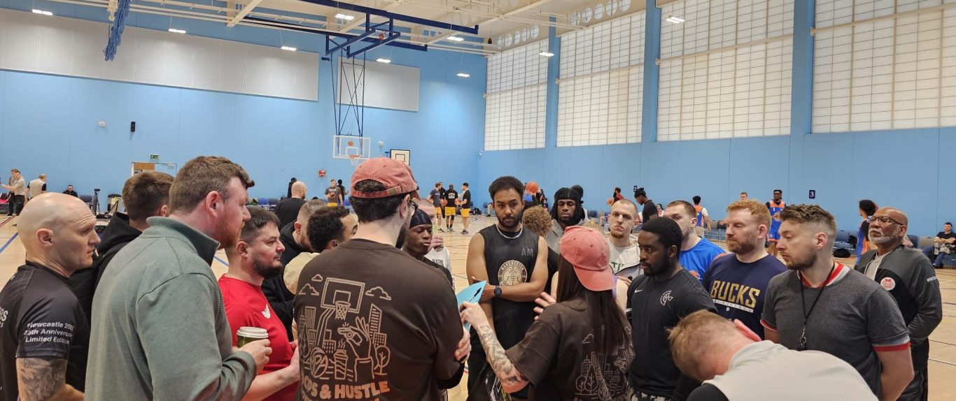 A group of diverse people gathered in a sports hall, engaged in discussion.