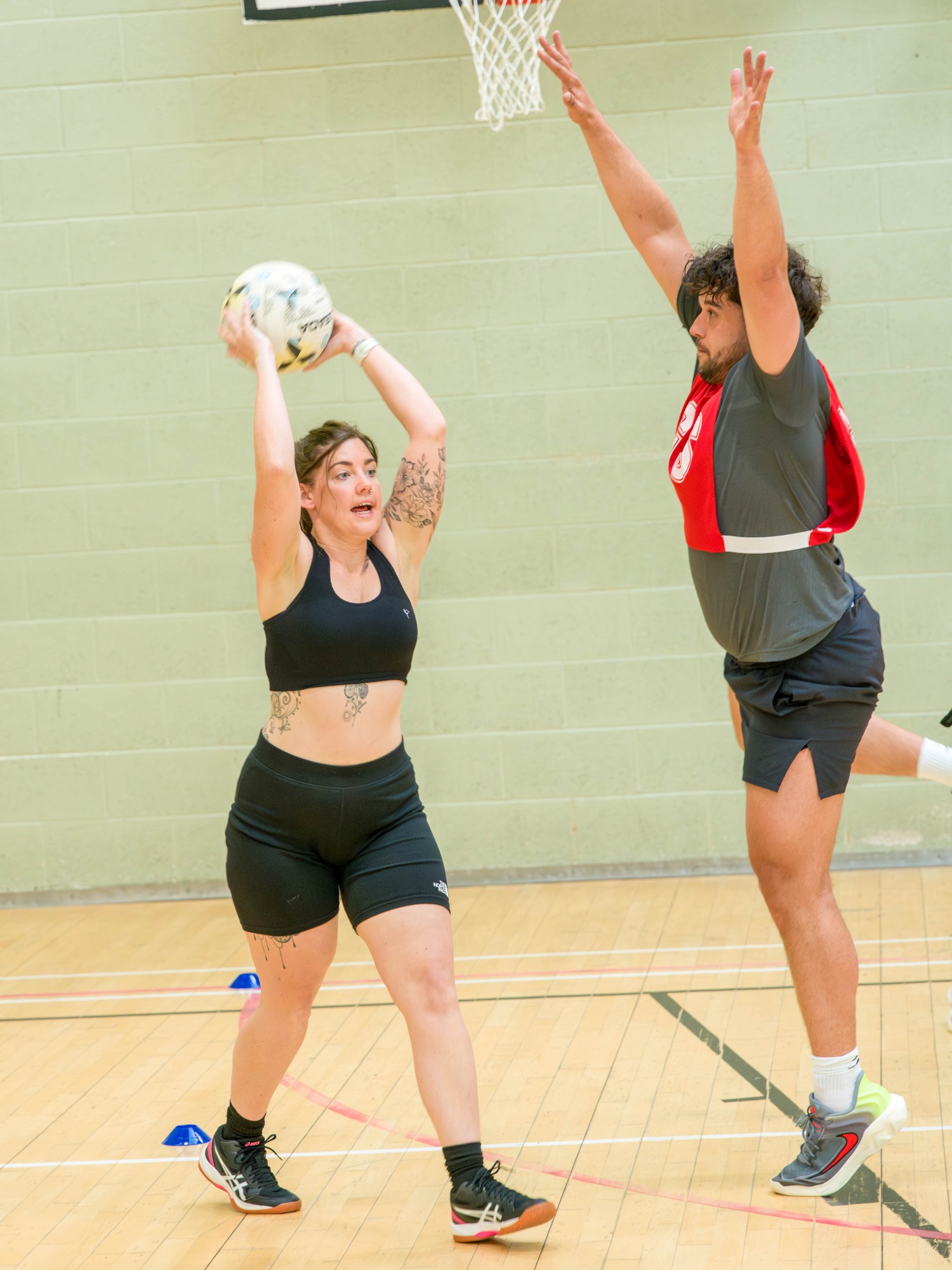 A woman in a sports bra prepares to pass a ball as a man jumps to block her.
