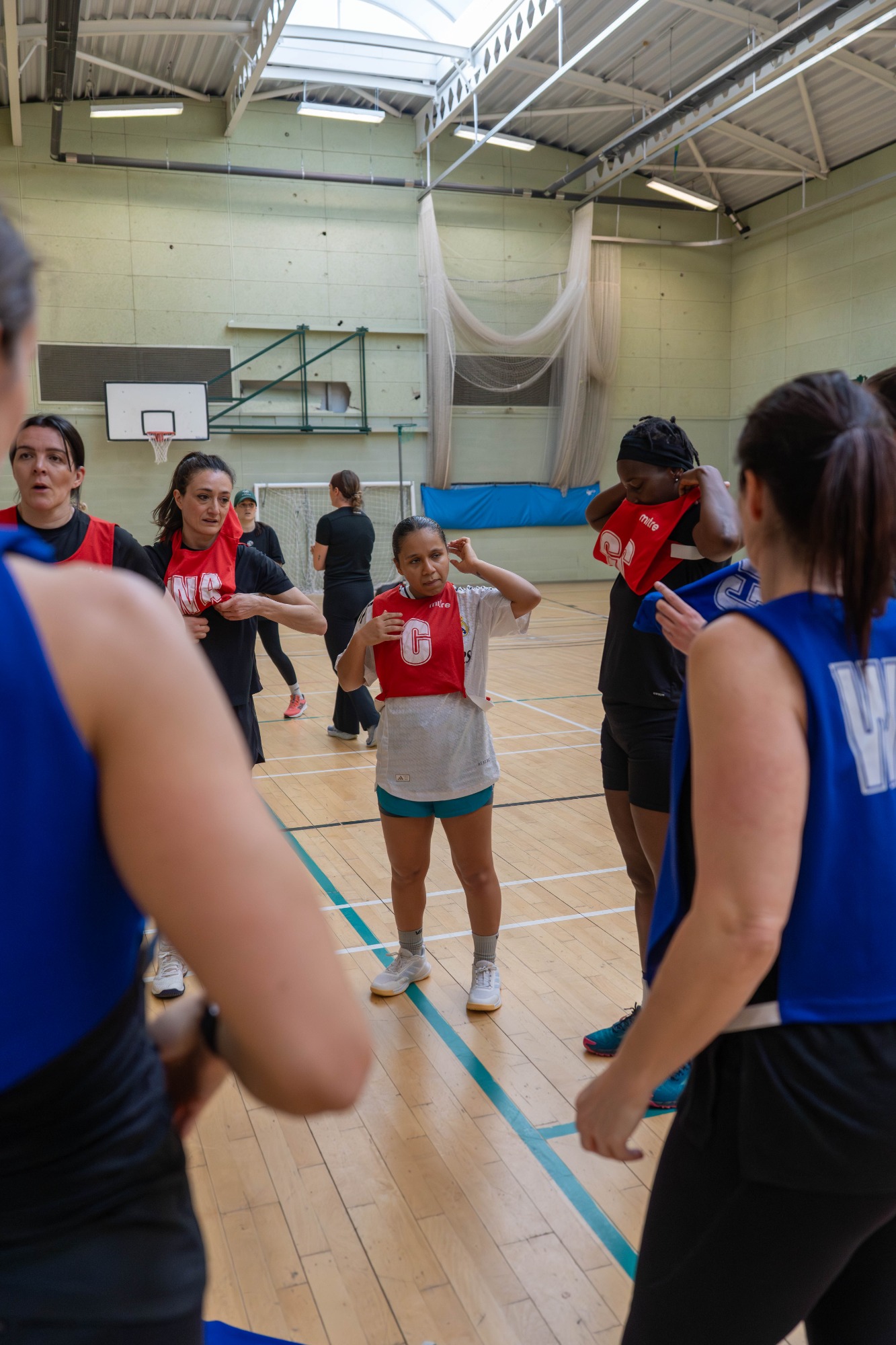 A basketball training session with players wearing red and blue jerseys in a gym.