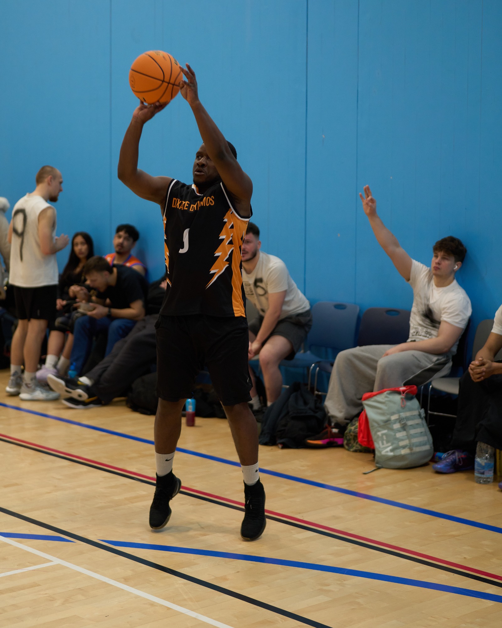 Player shooting a 3 point basketball shot with a member of the crowd signalling a 3 point shot with their hand.