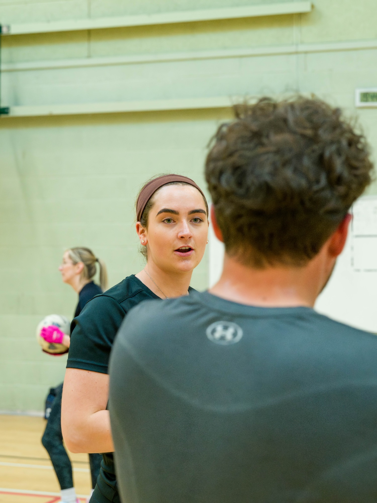 Two young people engaged in conversation in a sports hall, with a volleyball in the background.