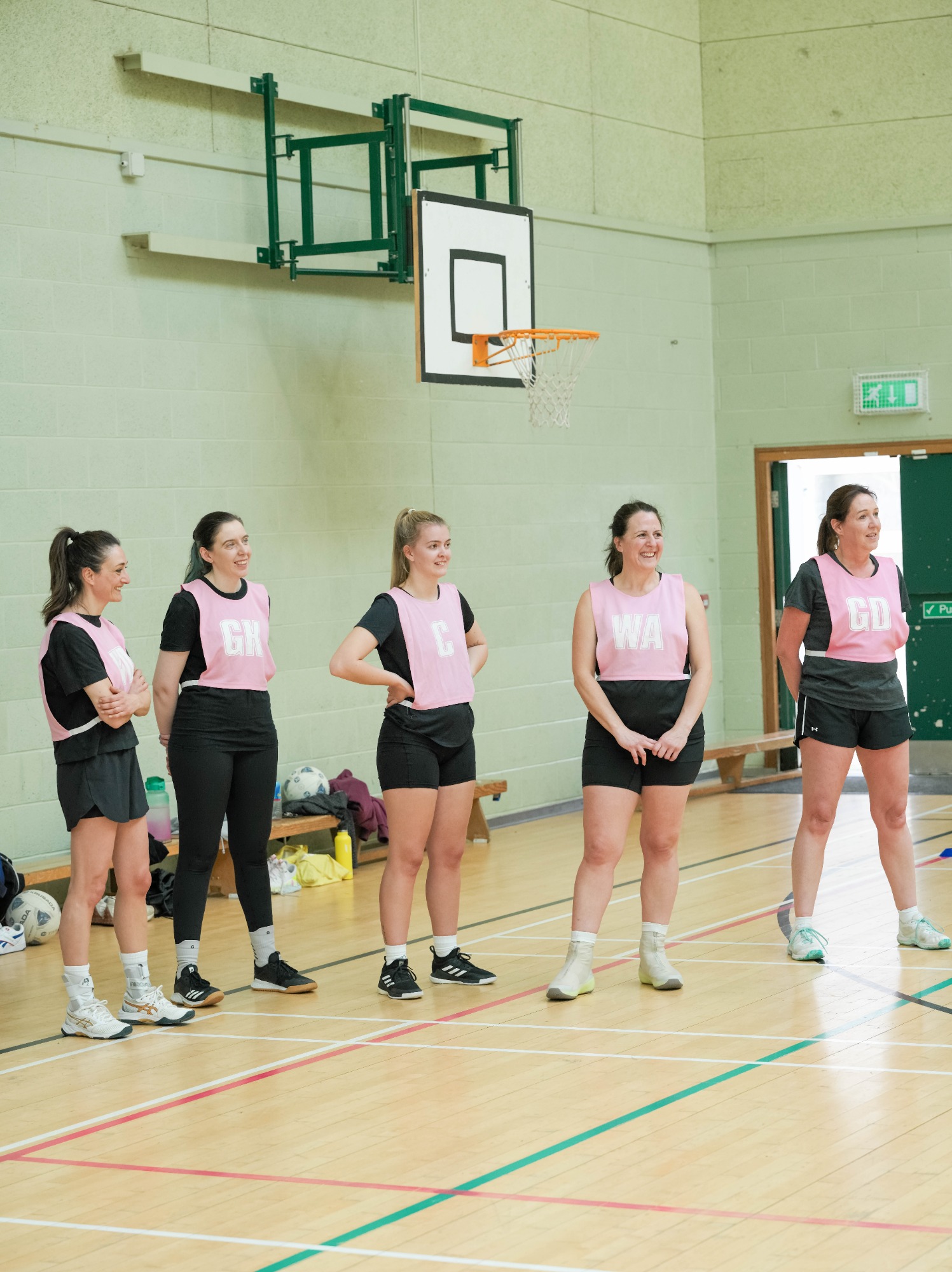 A group of five women in sportswear standing on a gym court, ready for a game.