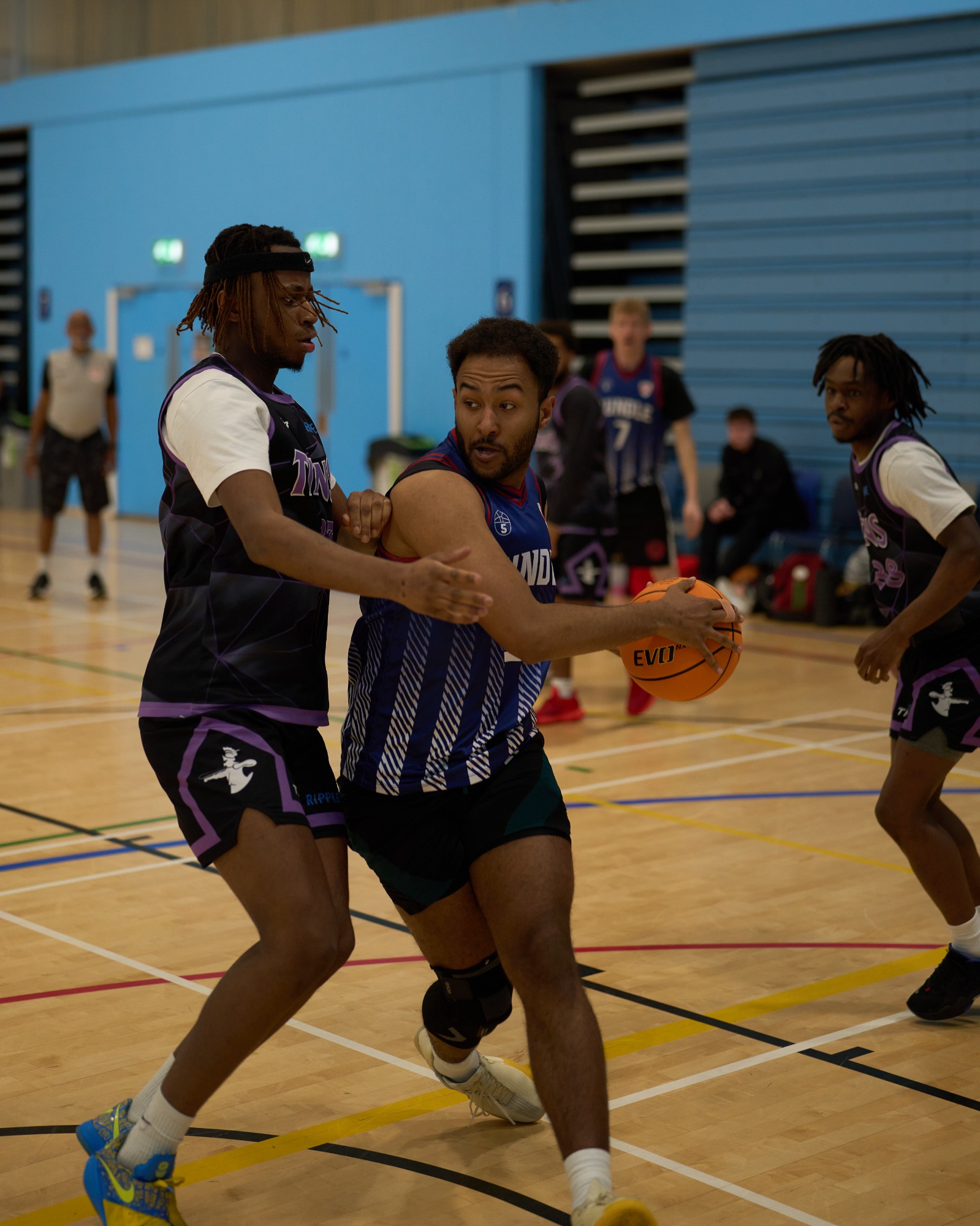 Player driving with the basketball on 1 leg whilst being defended from both sides.