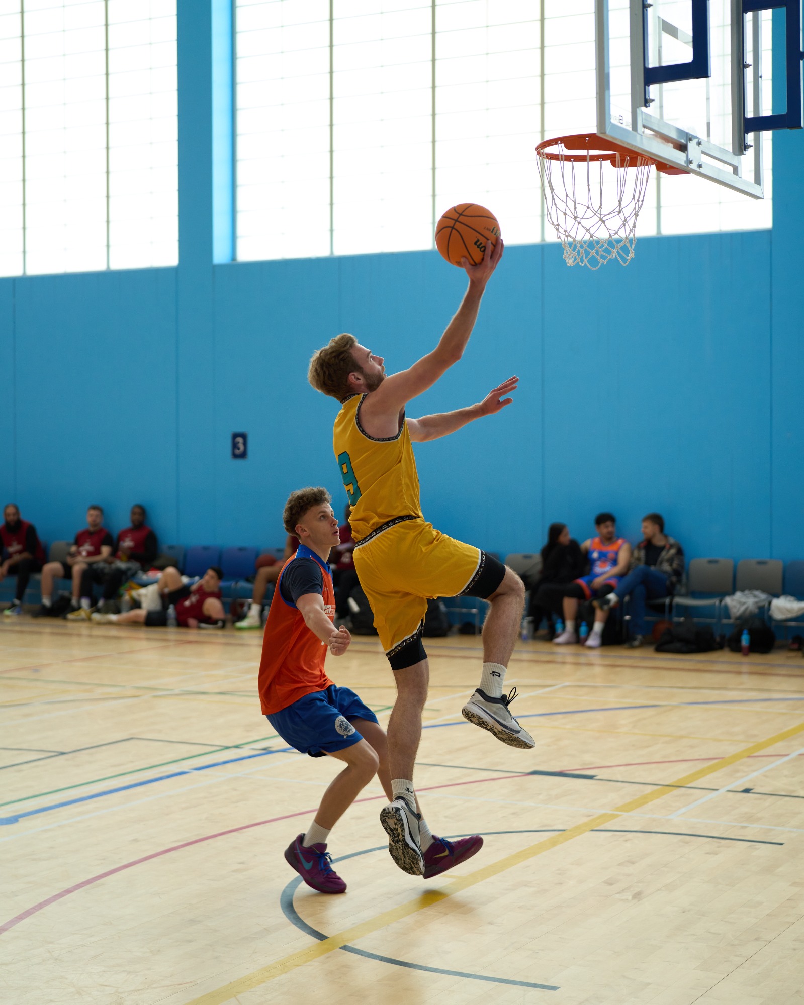 A basketball player leaps for a shot while a defender attempts to block.