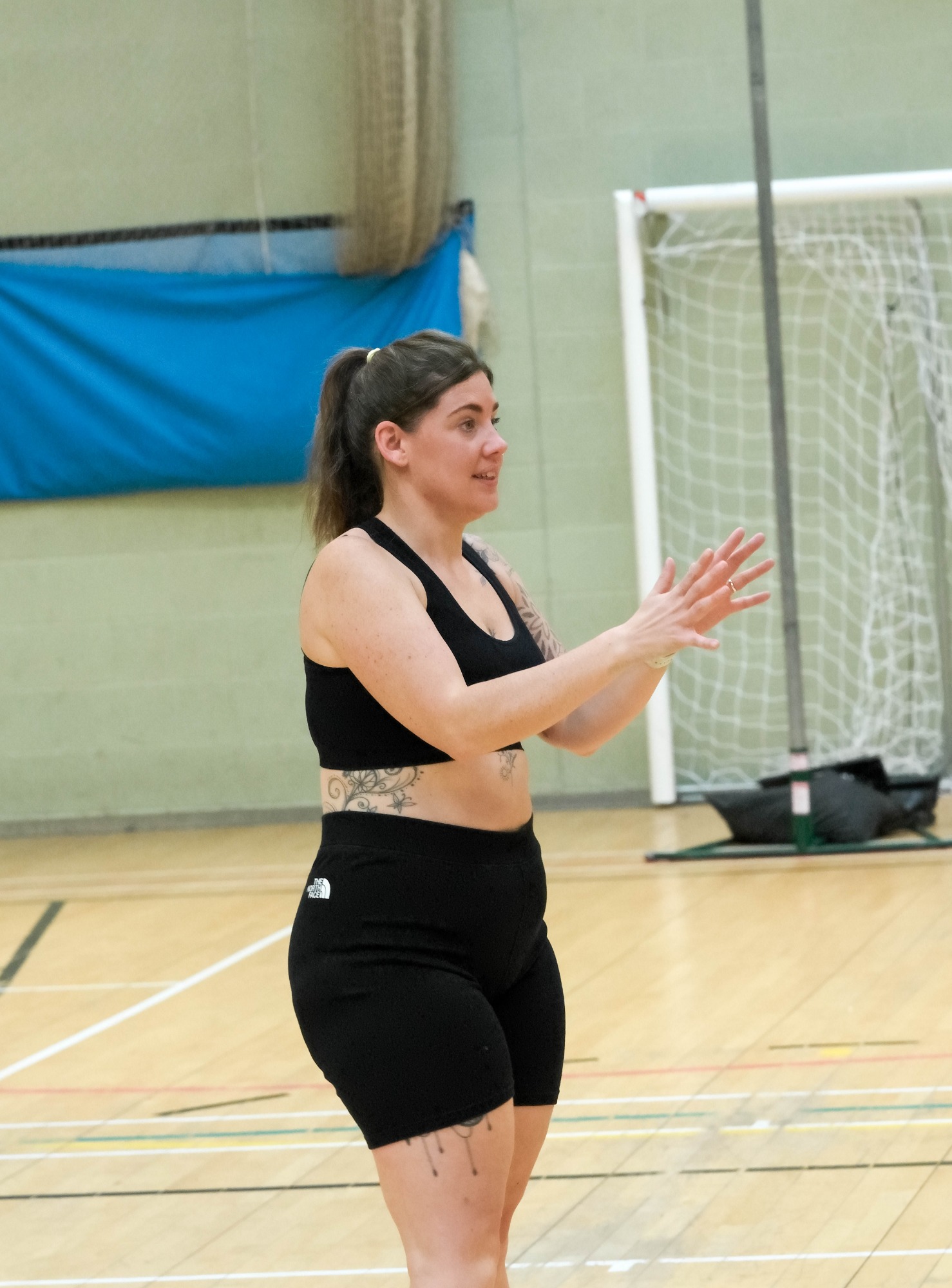 A woman in sportswear gestures enthusiastically on a gymnasium court.