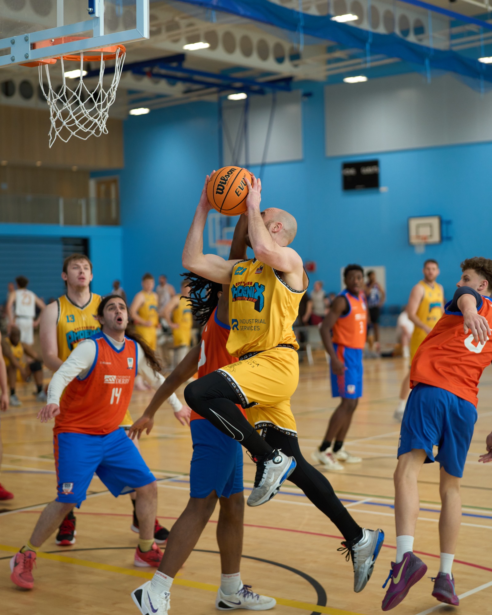 A player in a yellow jersey jumps to shoot a basketball during a match in a gym.
