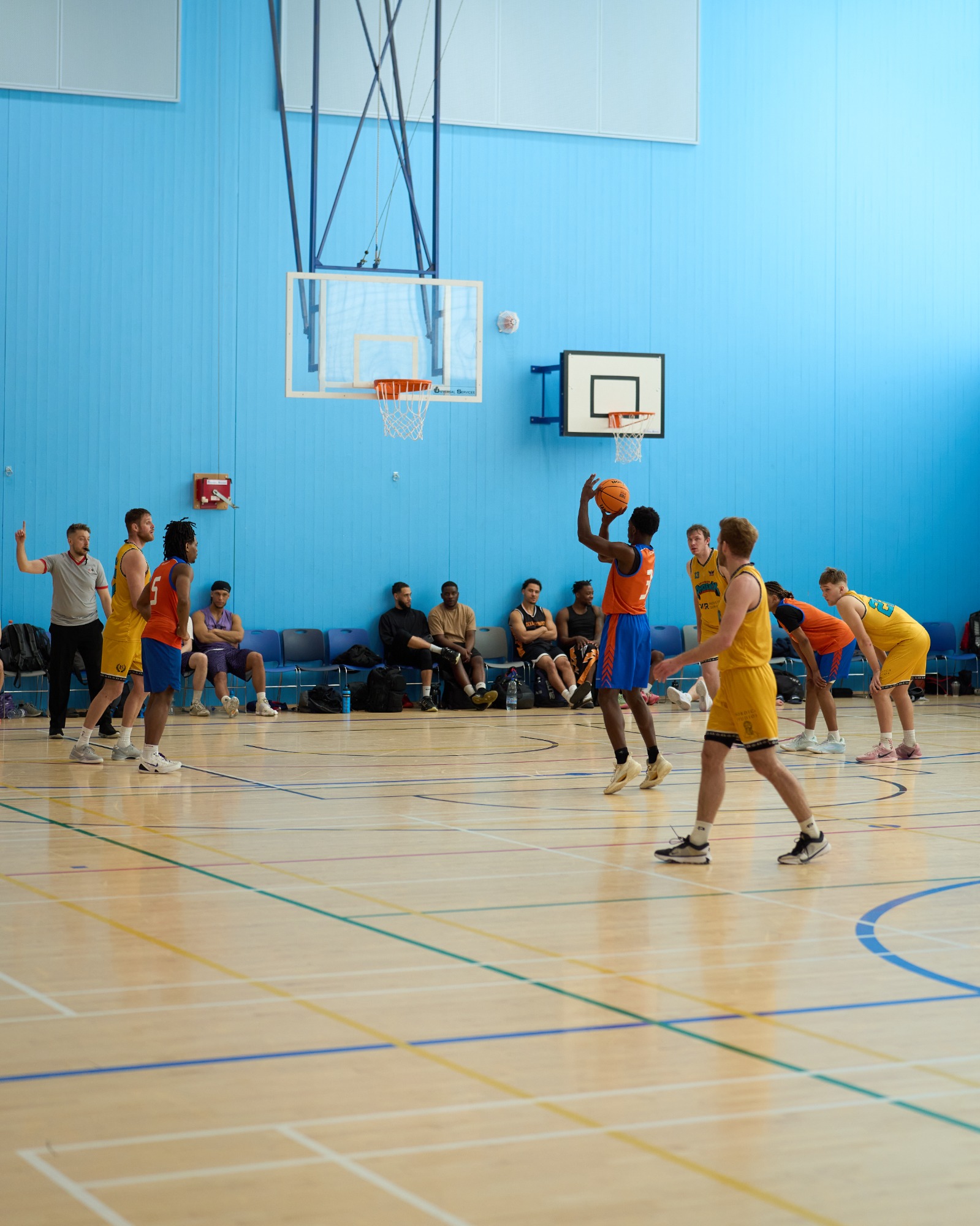 Players in blue and yellow jerseys compete in a basketball game indoors.