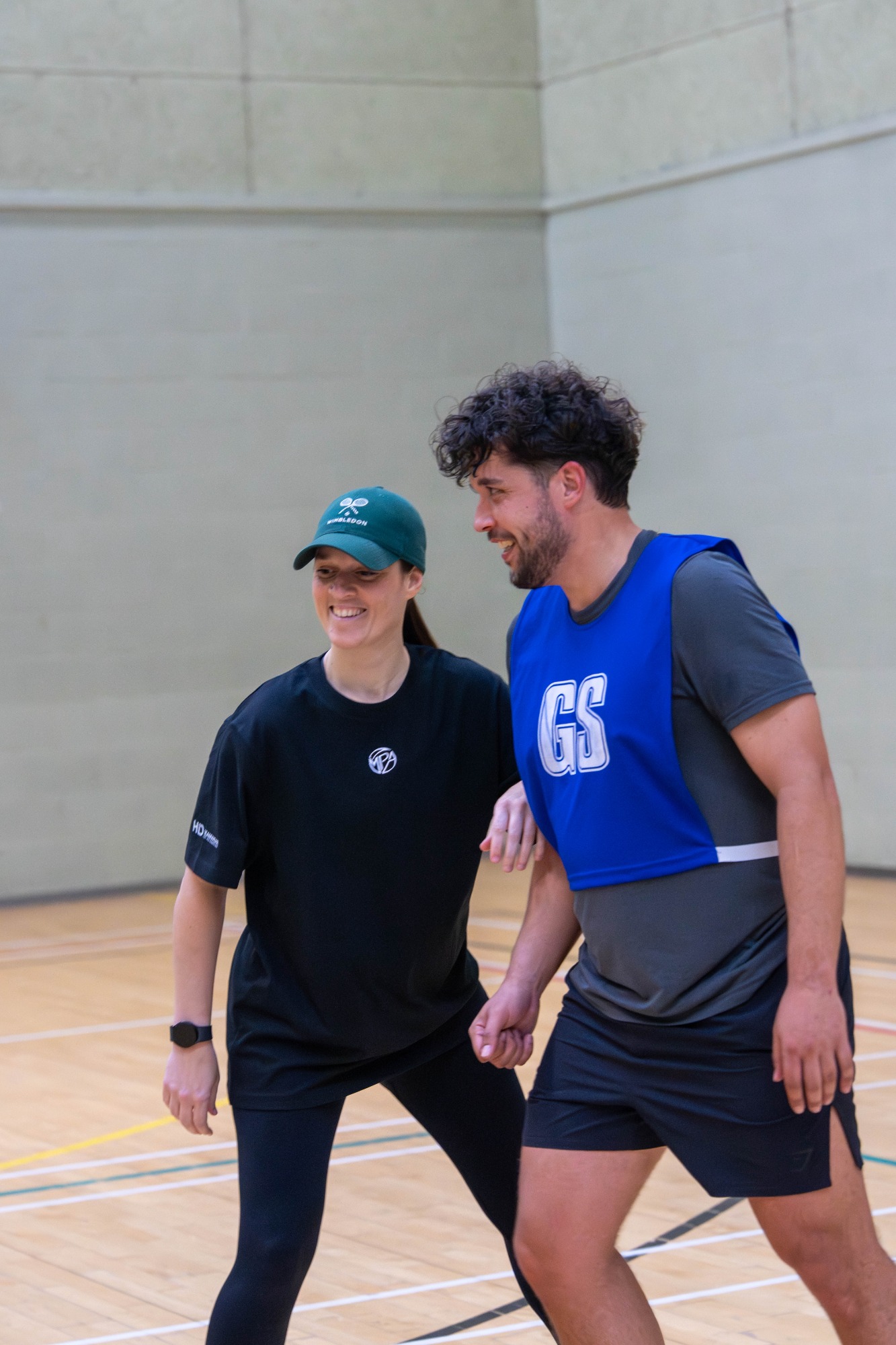 Two people engaged in a sports activity indoors, one wearing a blue bib and a cap.