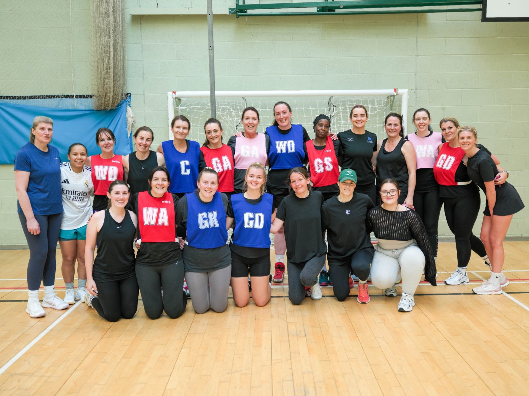 A group of women in sports attire, posing together on a netball court.
